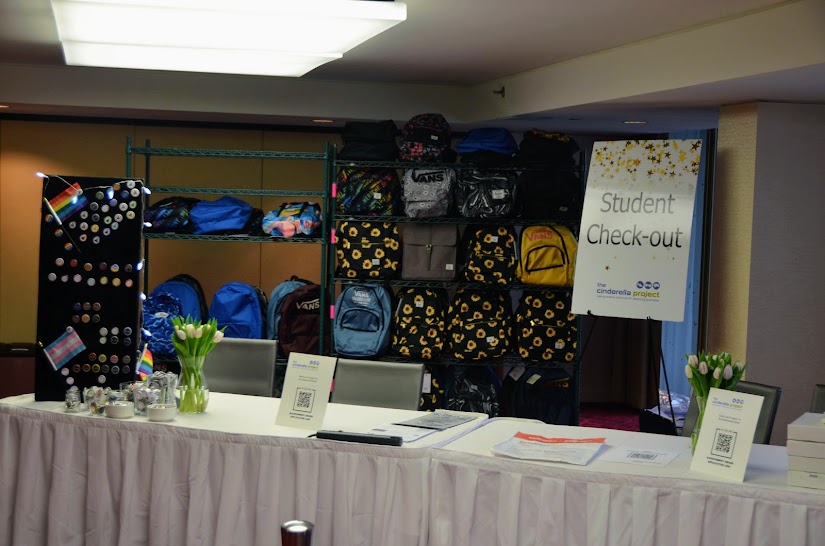 A table where students will check in for the event. Behind the table are many backpacks that students will get to take home at the end of the day.
